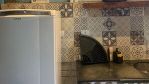 A kitchen with a refrigerator, a sink, a decorative wall with patterned tiles, a wall-mounted light fixture, and a small plant. - De Casa Eu Gosto (Ubatuba)