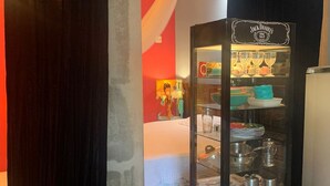 A room with a black curtain, a potted plant, a Jack Daniel's display cabinet, and a wooden table. - De Casa Eu Gosto (Ubatuba)