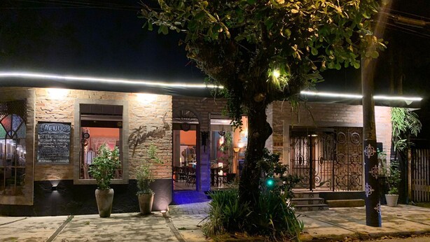 A restaurant with a stone facade, outdoor seating, and a tree in the foreground. - De Casa Eu Gosto (Ubatuba)