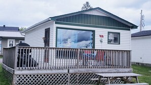 A small, single-story cabin with a fenced deck and a picnic table.