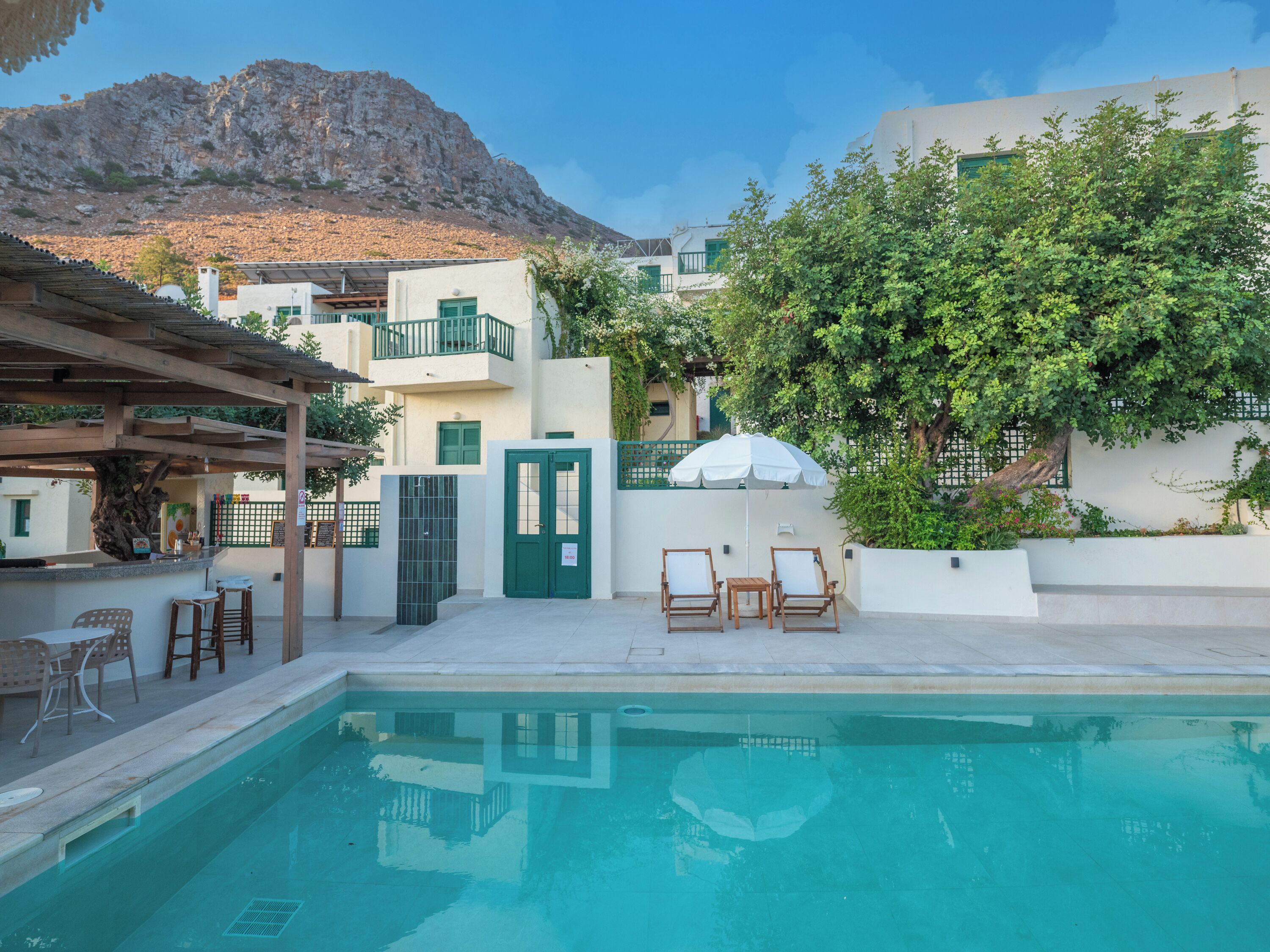 A pool area with a mountain backdrop, outdoor seating, and a building with a green door.