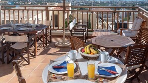 A terrace with outdoor seating, a table set for breakfast, and a view of the sea and cityscape. - Apartment with Sea View, Kalimera Village (Hersonissos)