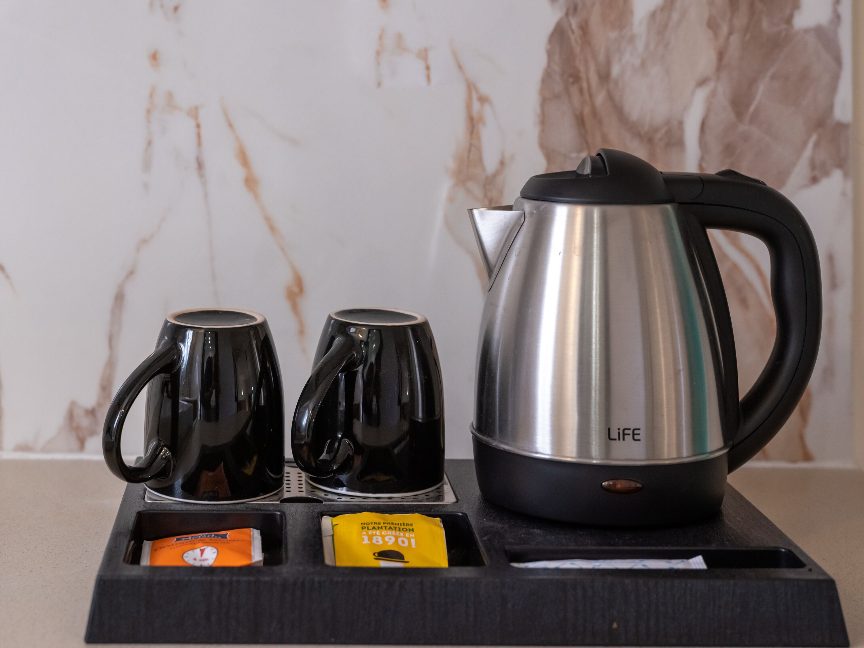 Un coin café avec deux tasses noires, une bouilloire argentée de la marque LIFE et deux paquets de café.