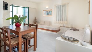 A modern living room with a dining area, a sofa, a small decorative tree, and a painting on the wall. - Apartment with Sea View, Kalimera Village (Hersonissos)