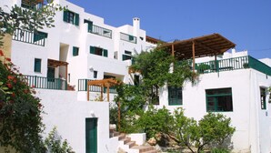 A white building with green shutters and balconies, featuring a stone staircase and a wooden pergola. - Apartment with Sea View, Kalimera Village (Hersonissos)