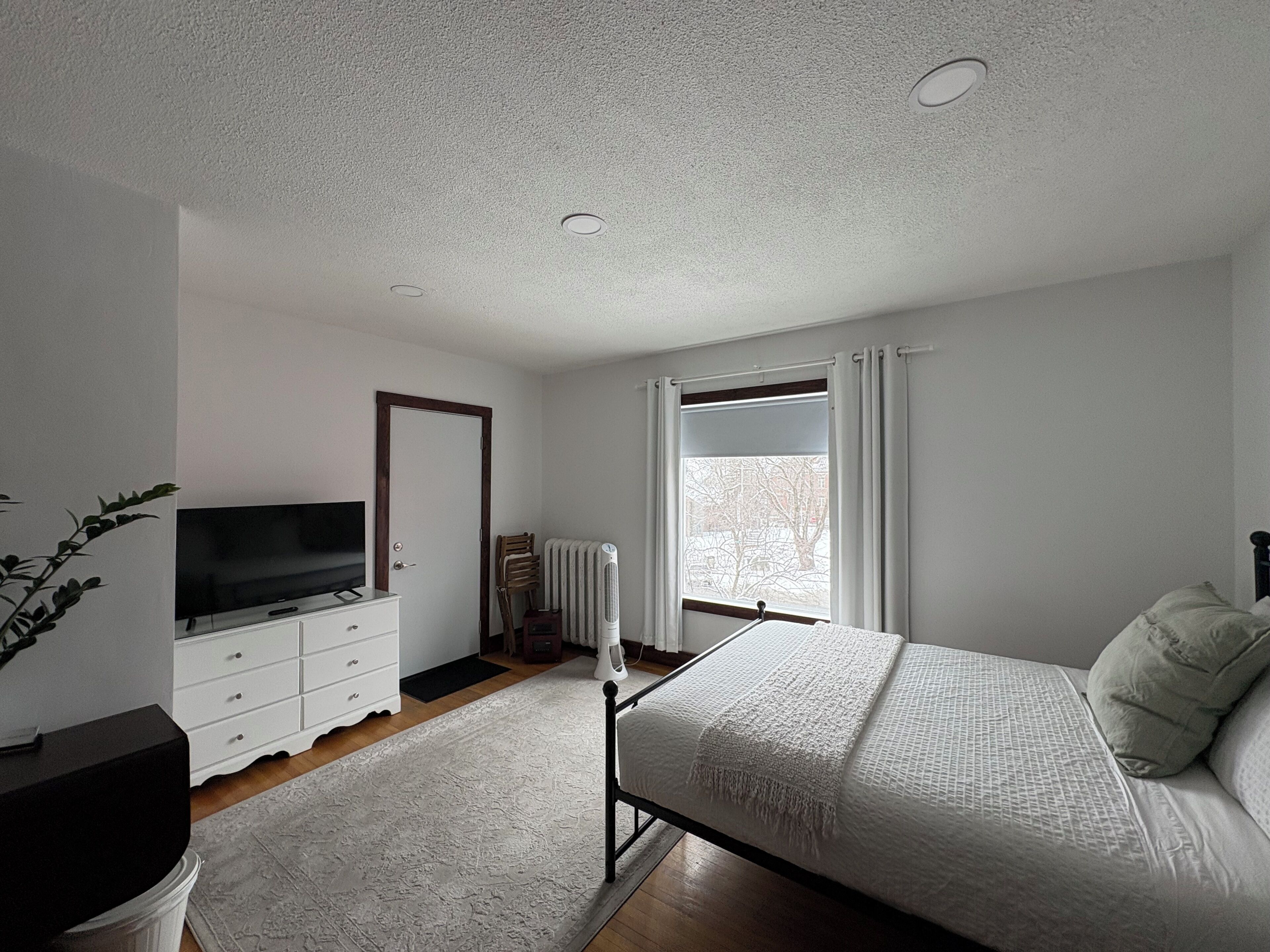 A bedroom with a bed, a dresser, a TV, a radiator, and a window.