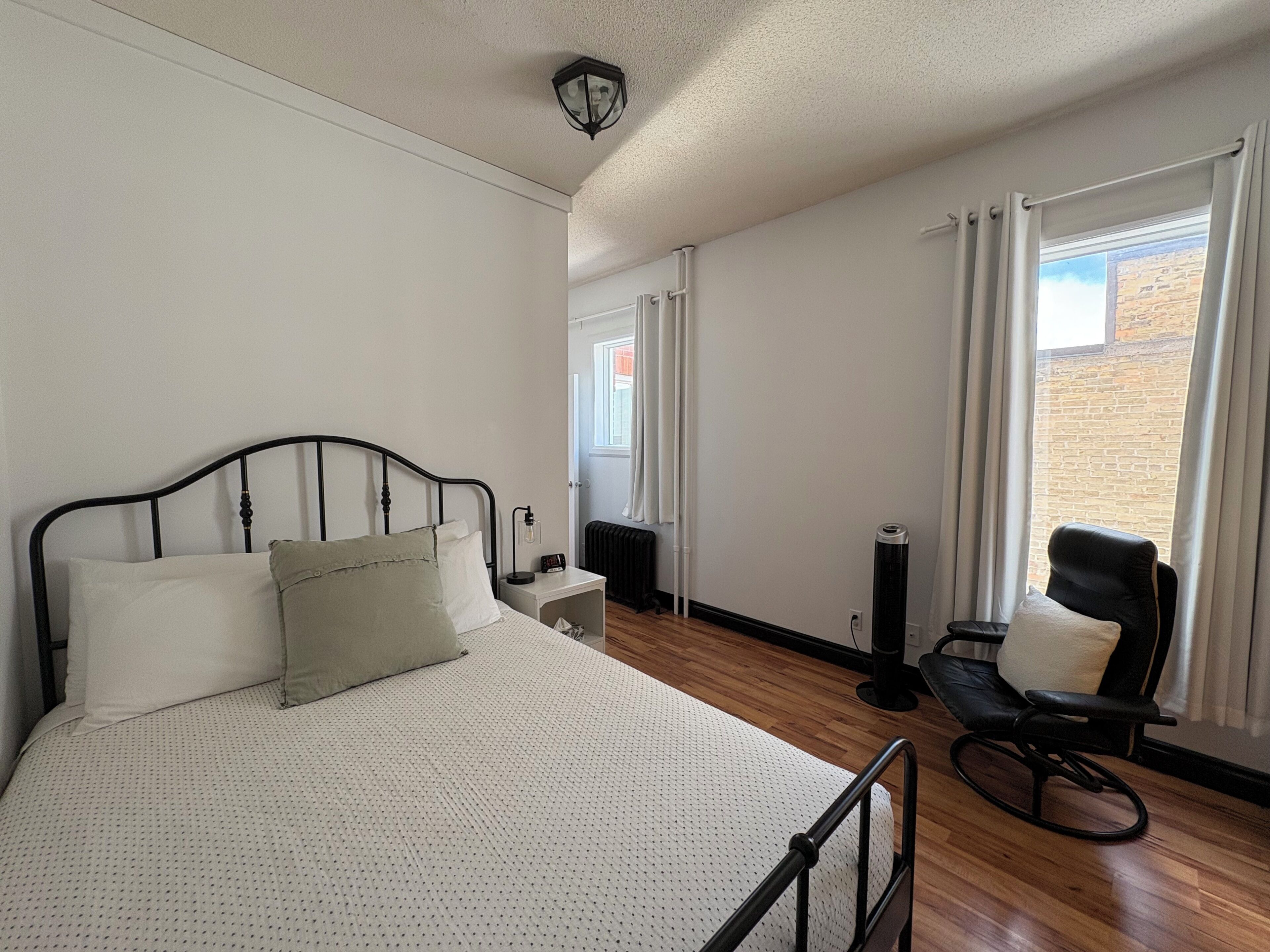 Une chambre à coucher comprenant un lit, une table de chevet, une chaise et donnant sur l’extérieur.