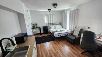 Una habitación de hotel pequeña con una cama, un escritorio, una silla, un lavamanos y una planta en maceta.
