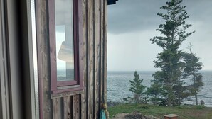A wooden cabin with a window overlooking a rocky garden and the sea. - Fundy Fantasy Oceanfront Cabin. Offgrid romantic getaway. (Granville Ferry)