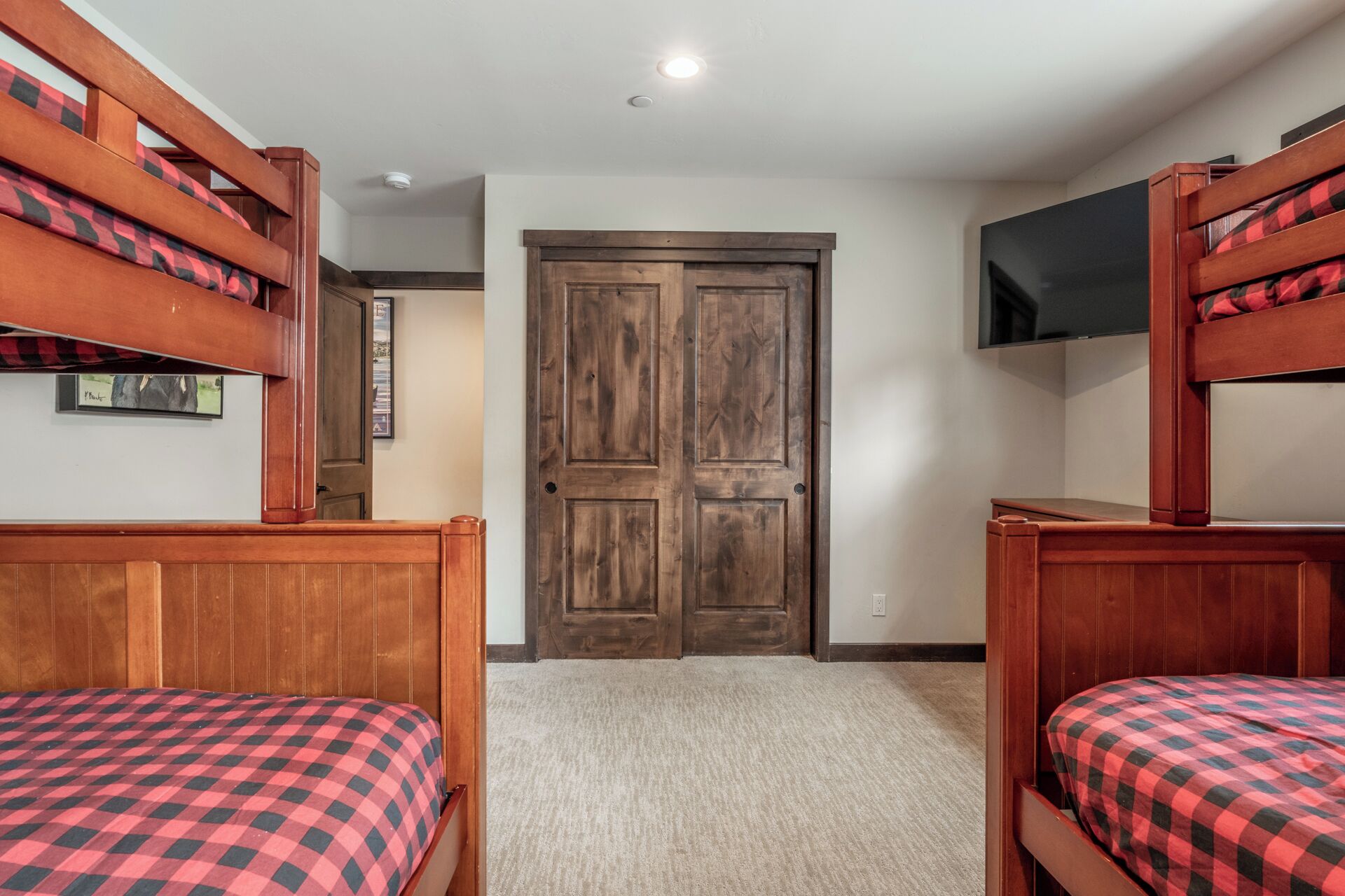 A room with bunk beds, a wooden door, a flat-screen TV, and a carpeted floor.