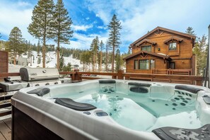 Een houten chalet met een jacuzzi en een barbecue op het terras.