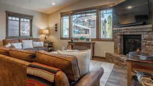Un salón acogedor con chimenea de piedra, sofás de cuero y grandes ventanales con vistas a una cabaña de madera.