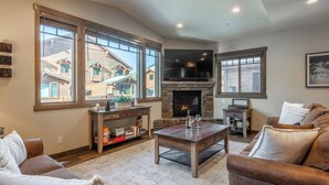 Un salón acogedor con chimenea, ventanas amplias, un televisor de pantalla plana y asientos cómodos.