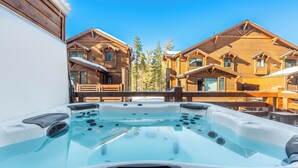 Un jacuzzi con panel de control mostrando 39 grados Celsius, rodeado de cabañas de madera con nieve en el techo.