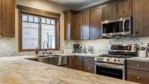 Una cocina con armarios de madera, un lavamanos de acero inoxidable, un microondas, una estufa y una ventana con persianas.