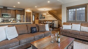 A spacious living area with a large brown sofa, a wooden coffee table, and a dining area in the background.