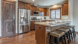 A modern kitchen with wooden cabinets, stainless steel appliances, a marble countertop, and a bar area with stools.
