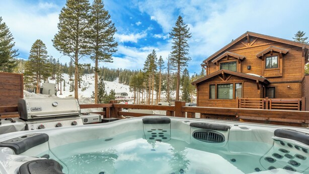 A hot tub with a wooden deck and a wooden cabin in the background.