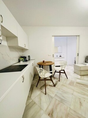Een moderne keuken met witte kasten, een zwarte kookplaat en een ronde houten tafel met twee witte stoelen.