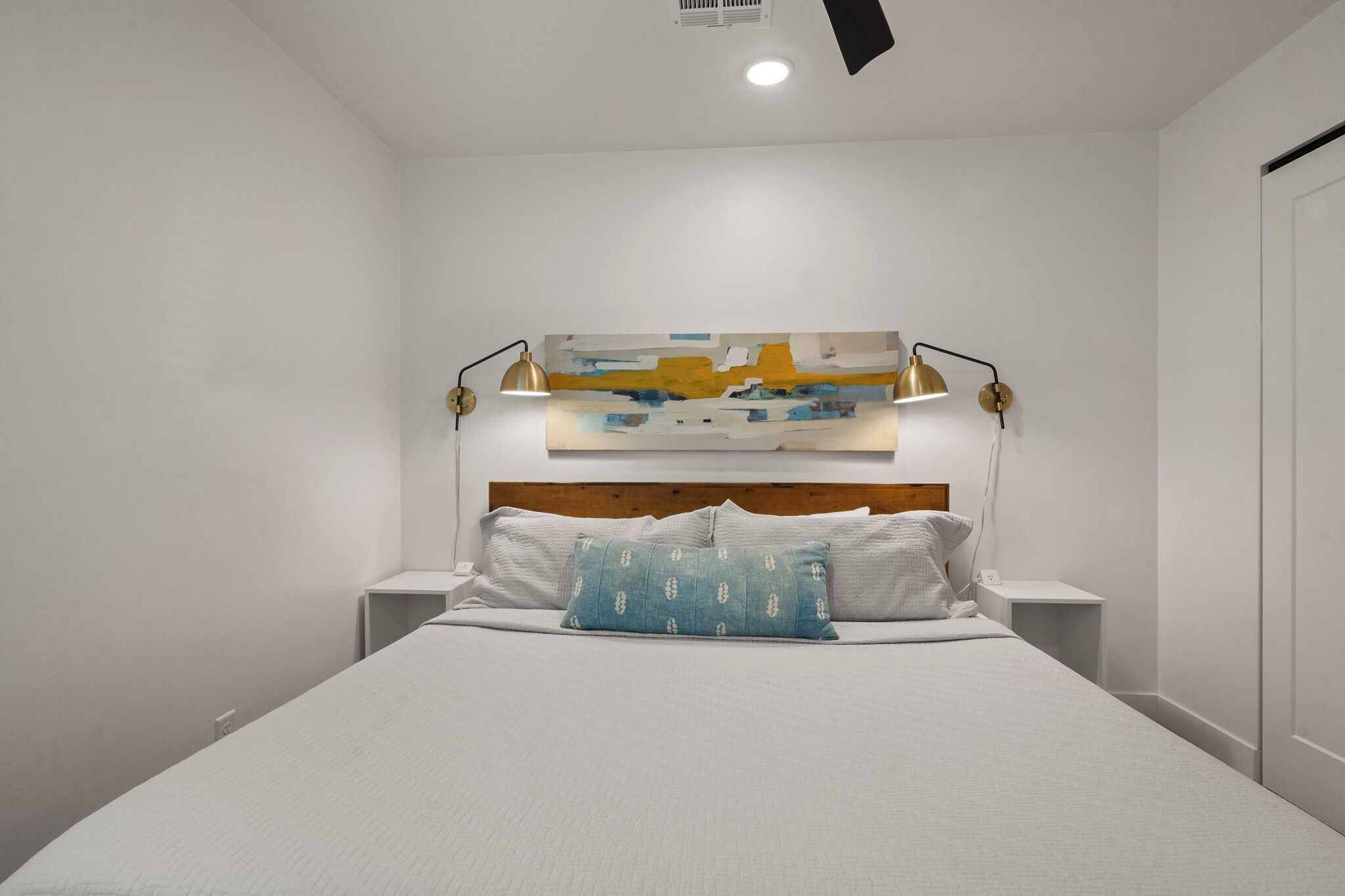Un dormitorio moderno con una cama grande, dos mesitas de noche, un cabecero de madera y un cuadro abstracto colgado en la pared.