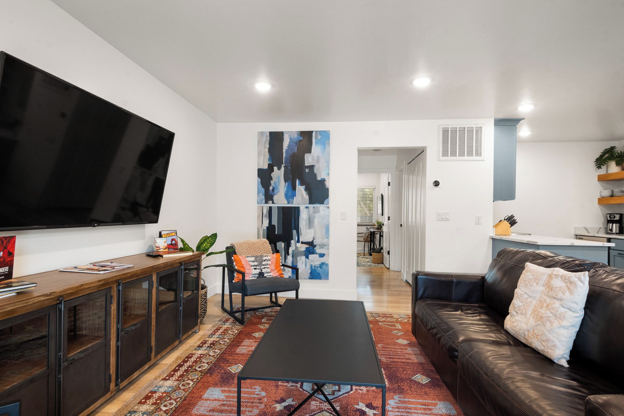 A modern living room with a flat-screen TV, a black coffee table, a leather sofa, and a patterned rug.