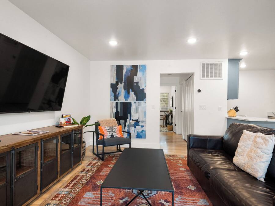 A modern living room with a flat-screen TV, a black coffee table, a leather sofa, and a patterned rug.