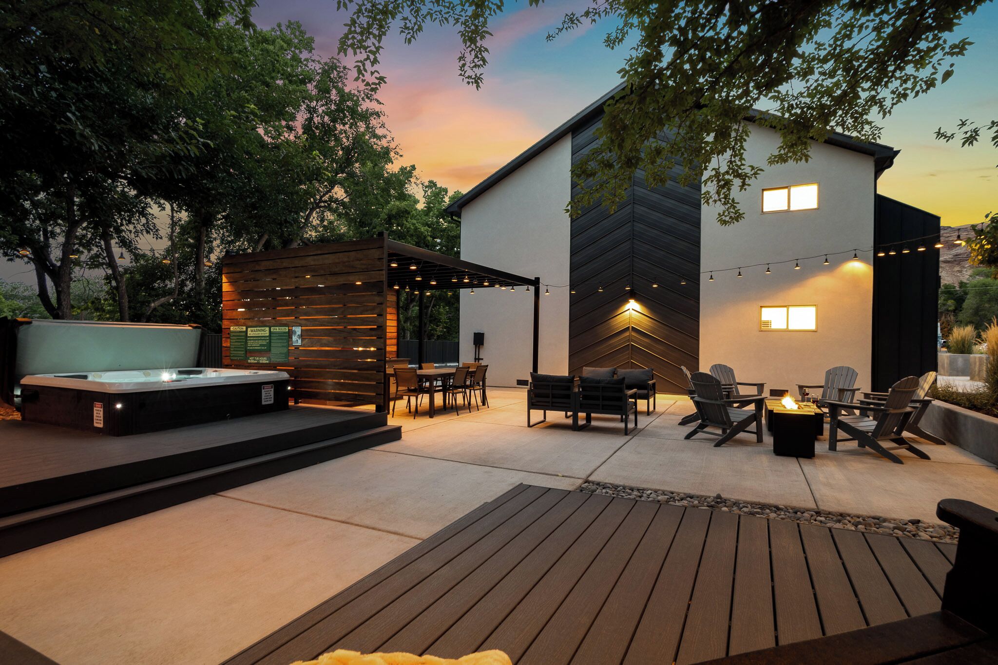 A modern outdoor patio with a hot tub, seating area, and string lights.