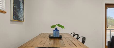 A dining area with a wooden table, black chairs, and a blue vase with a plant.