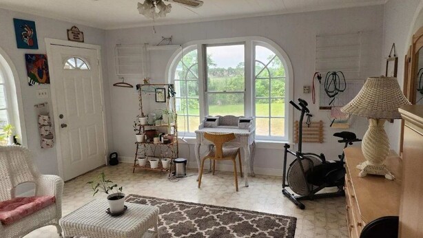 A cozy room with a large window, a wicker chair, a small table, and a stationary exercise bike.