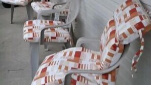 A row of outdoor lounge chairs with checkered cushions, positioned against a building with horizontal siding and windows.