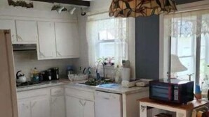 A kitchen with white cabinets, a sink, a microwave, and a hanging light fixture.