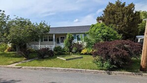 A two-story house with a front porch, surrounded by a well-maintained lawn and various shrubs.