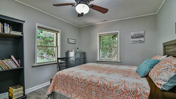 Un dormitorio con cama, estantería, escritorio y dos ventanas.