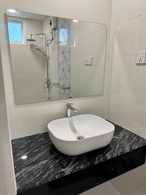 A modern bathroom with a large mirror, a white sink, and a shower.