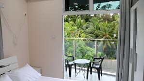 Ein Hotelzimmer mit Bett, einem kleinen Tisch, zwei Stühlen und einem Balkon mit Blick auf Grünflächen.