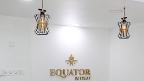Eine Rezeption mit einem Schild, auf dem 'Equator Retreat' steht. Zwei Pendelleuchten hängen von der Decke.