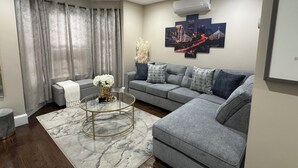 Un soggiorno moderno con un divano grigio, un tavolino in vetro e un quadro raffigurante un panorama cittadino.
