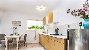 A modern kitchen with wooden cabinets, a stainless steel refrigerator, and a dining area with wicker chairs and a white table.