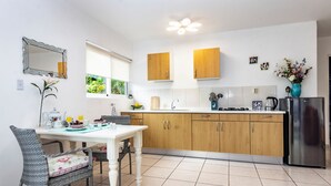 A modern kitchen with wooden cabinets, a stainless steel refrigerator, and a dining area with a white table and wicker chairs.