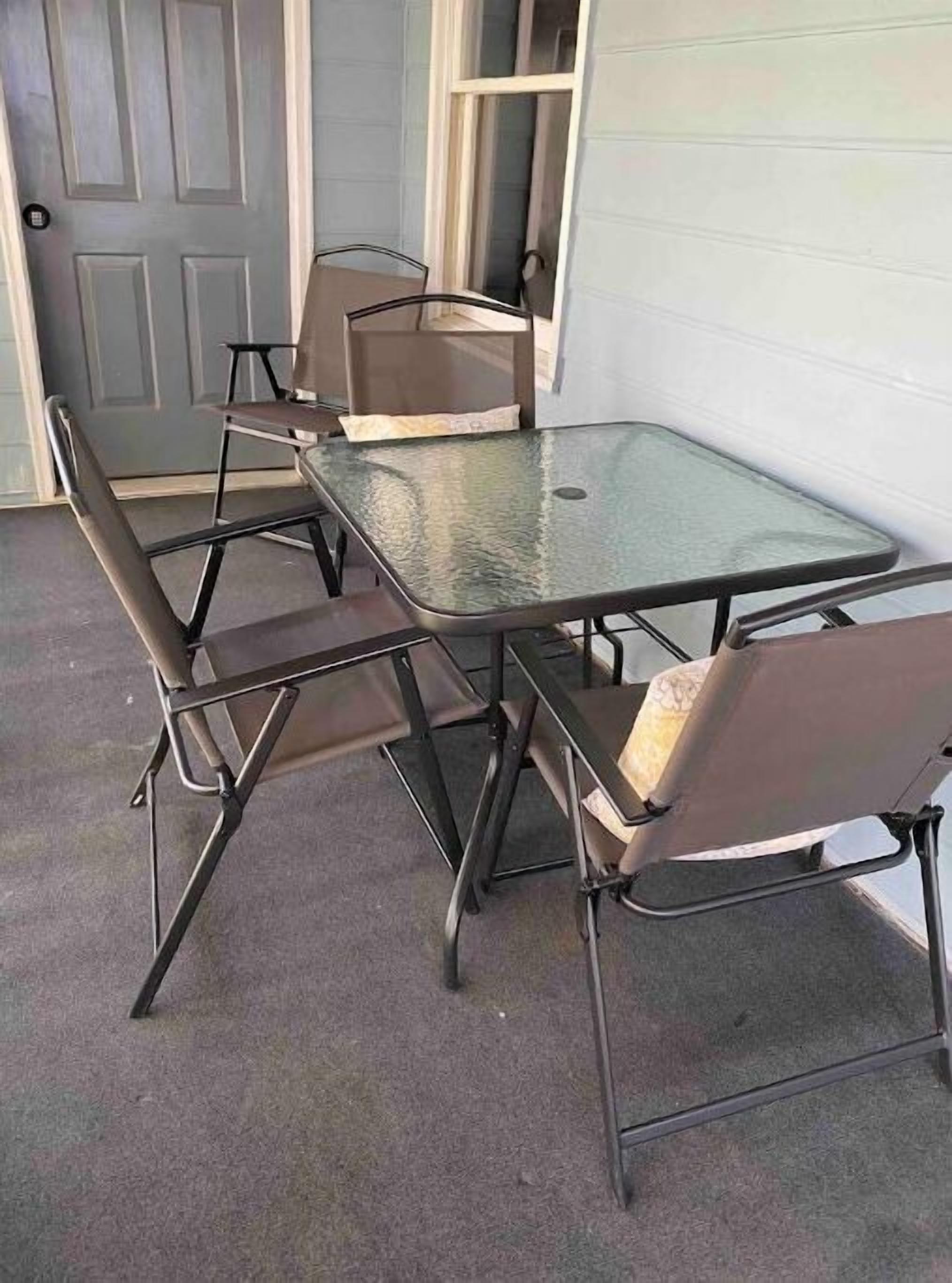 A metal-framed table with four chairs, a glass top, and a concrete floor.