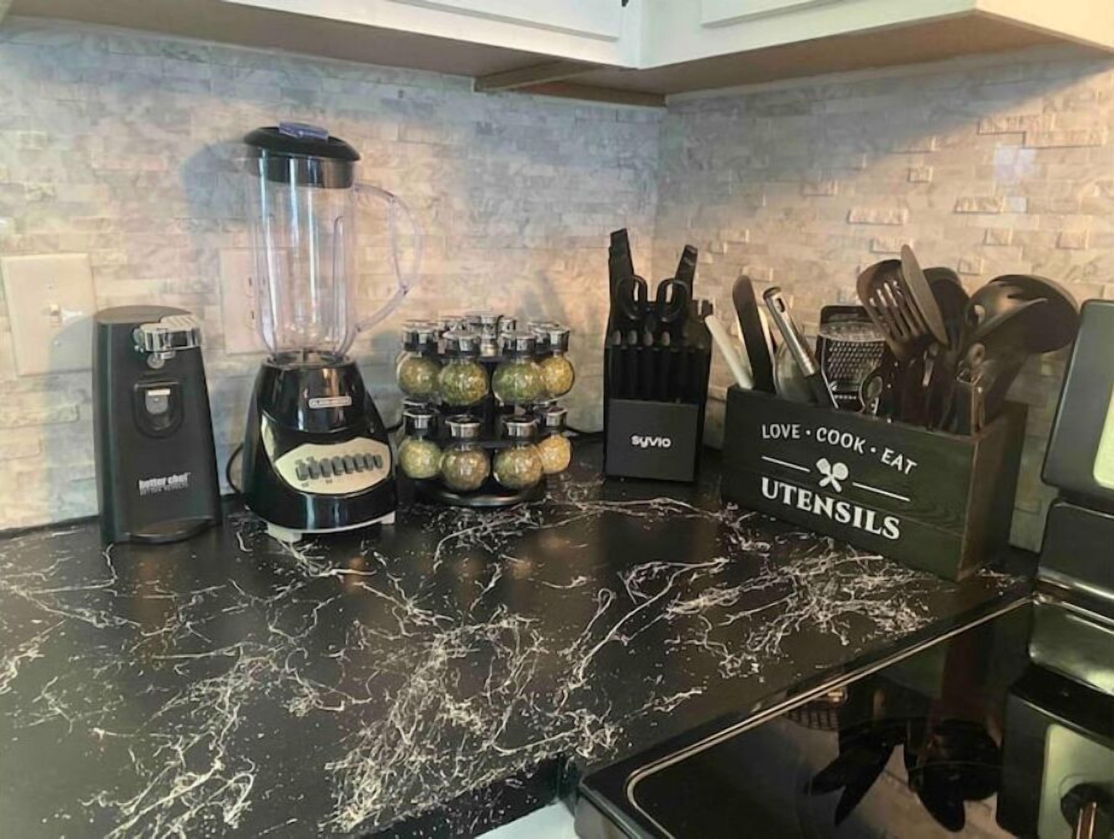 Una cocina con encimera de mármol negro, una licuadora, un extractor de jugos, un bloque de cuchillos y un recipiente para utensilios.