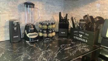 Una cocina con encimera de mármol negro, una licuadora, un extractor de jugos, un bloque de cuchillos y un recipiente para utensilios.