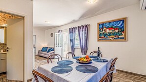 A dining area with a table set for four, a painting on the wall, and a view of the outside through a window. - Gorgeous apartment in Potomje with house sea view (Potomje)