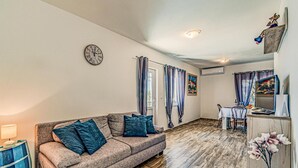 A living room with a sofa, a dining table, and a TV. - Gorgeous apartment in Potomje with house sea view (Potomje)