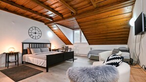 Een knus slaapkamer op zolder met schuine wanden, een bed, een slaapbank en een televisie.