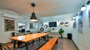 Een eetgedeelte met een houten tafel en bankjes, een aan de muur bevestigde televisie en decoratieve spiegels.