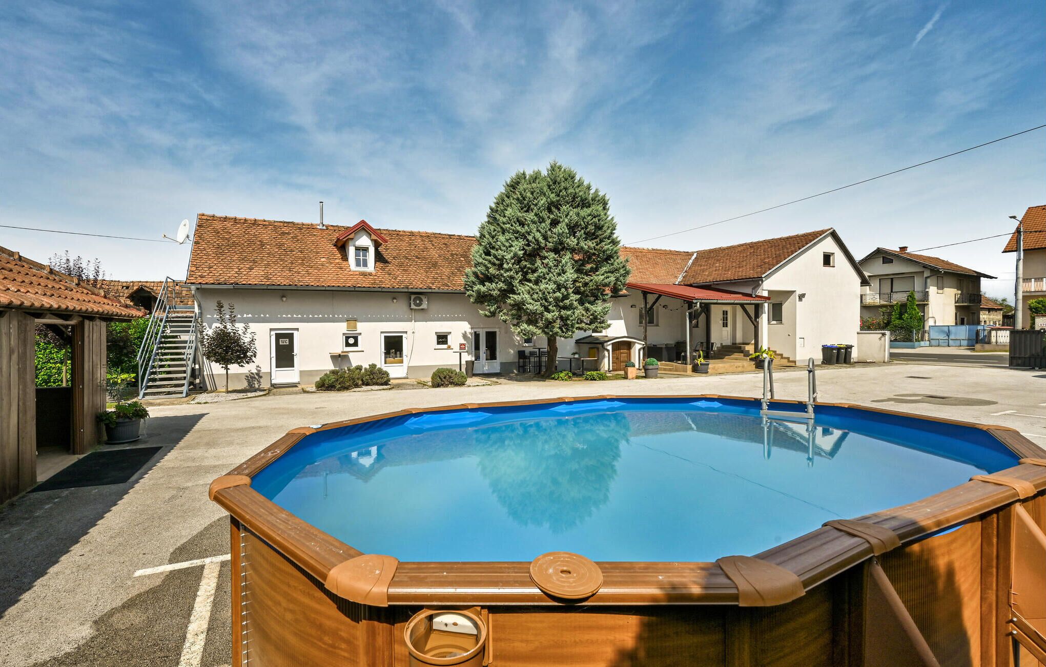Ein Schwimmbad mit Holzterrasse, umgeben von Häusern mit roten Ziegeldächern und einem großen Baum in der Mitte.