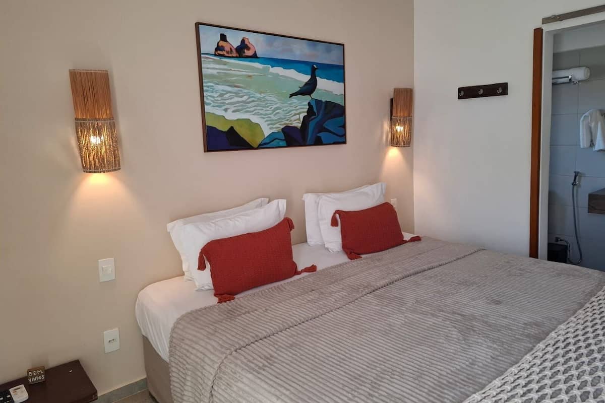 Une chambre à coucher avec un lit, deux lampes fixées au mur, un tableau et une porte donnant sur une salle de bain.