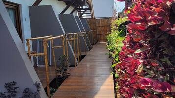 A wooden pathway leading to a building with a balcony, surrounded by lush greenery and a clear sky.