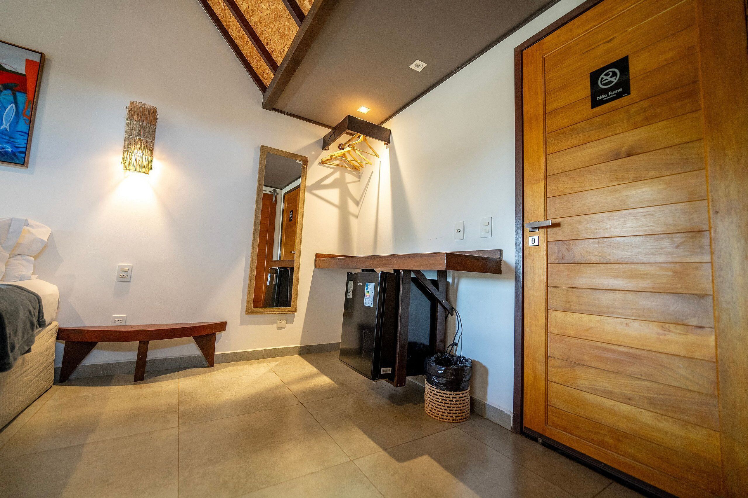A hallway with a wooden door, a bench, a wall-mounted light fixture, and a refrigerator under a counter.